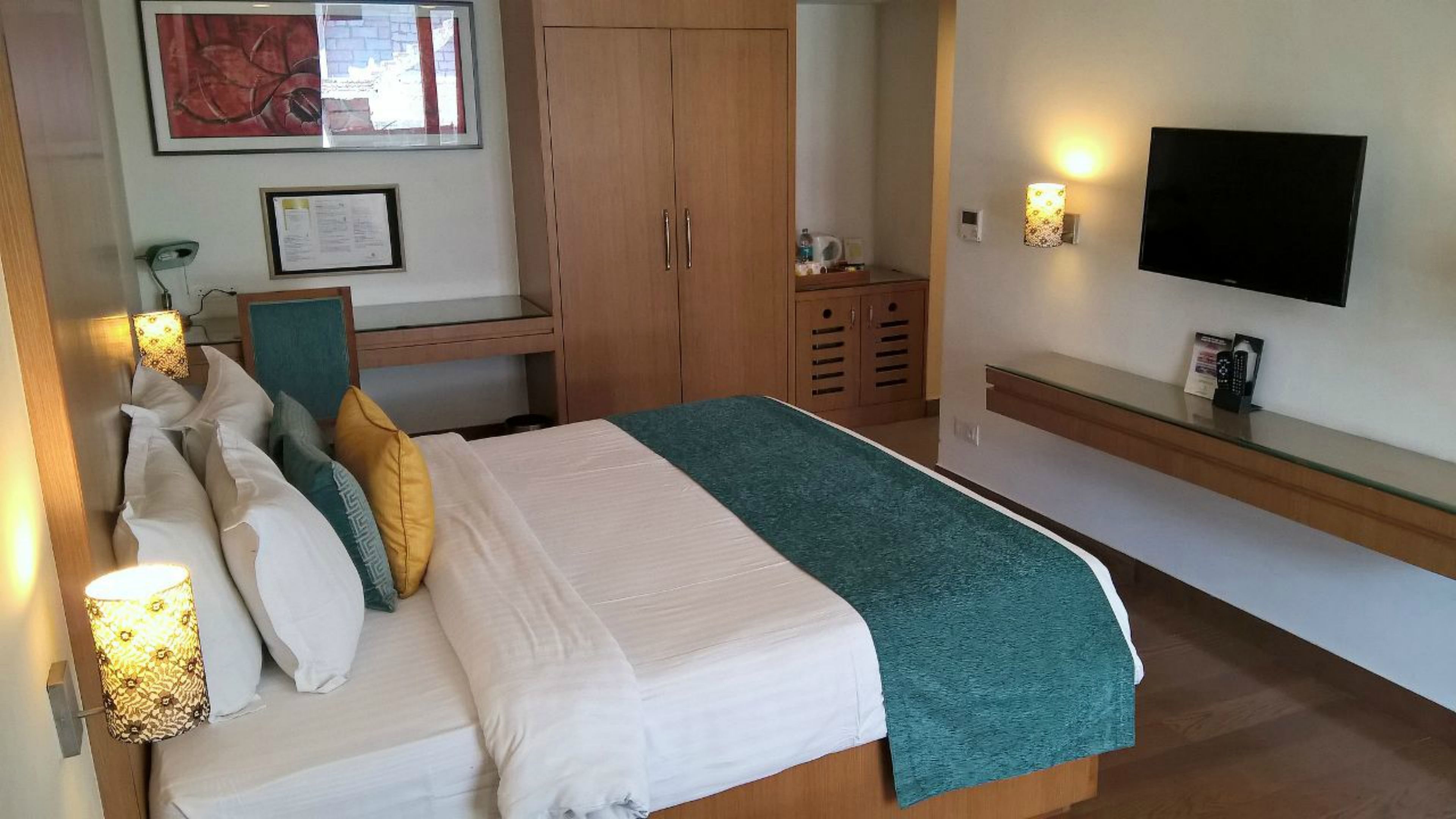 A hotel room with a bed, a desk, a wardrobe, a TV, and a wall-mounted lamp.