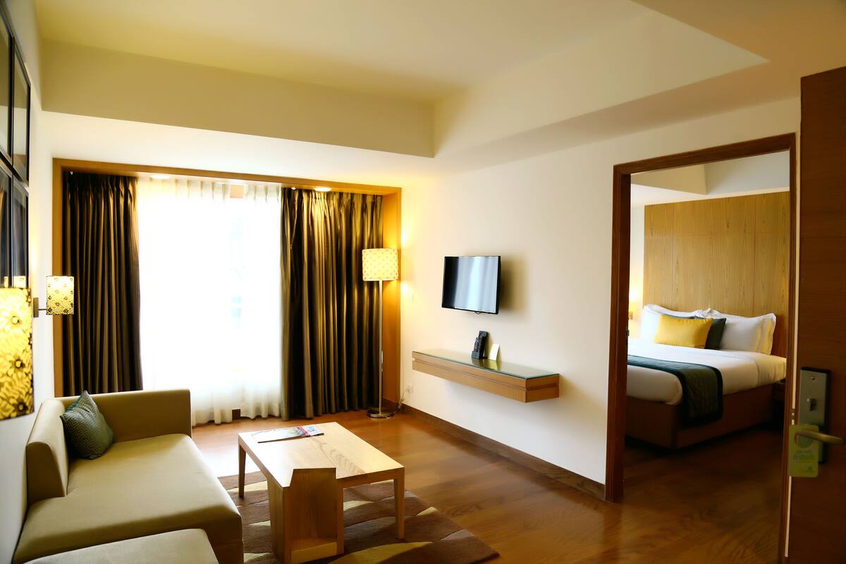 A hotel room with a sofa, a table, a TV, a bed, and a window with curtains.
