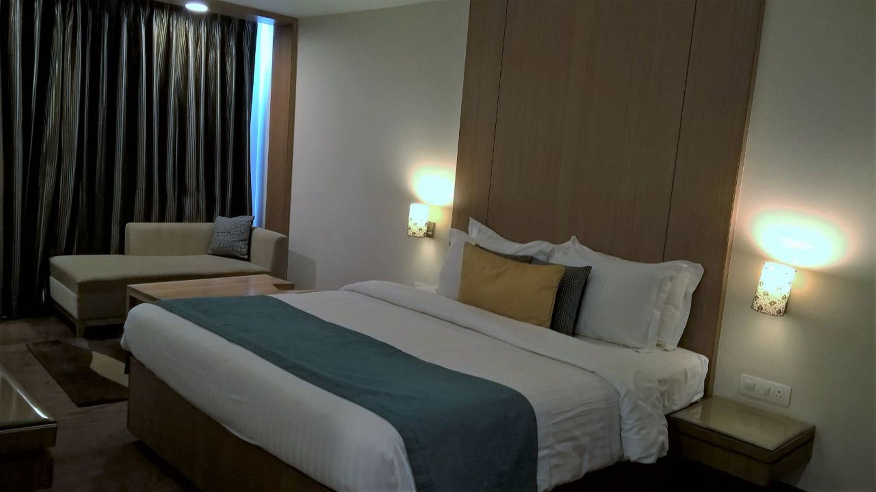 A hotel room with a large bed, a sofa, a nightstand, and a wall-mounted lamp.