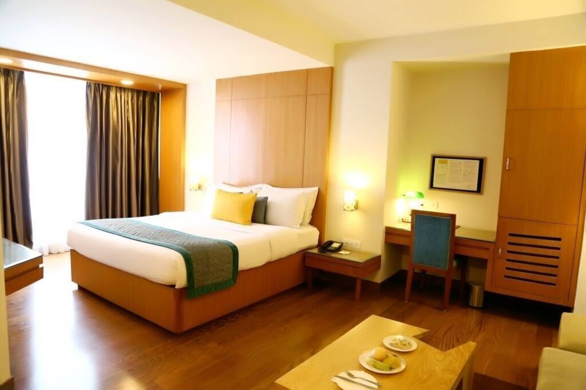 A hotel room with a bed, bedside table, desk, chair, and a dining table with plates.