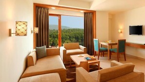 Une chambre d’hôtel moderne, équipée d’un canapé, d’une petite table, d’une télévision et offrant une vue sur une zone boisée.