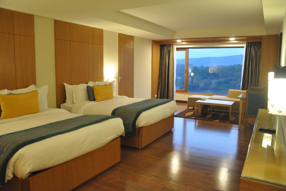 A hotel room with two beds, a desk, and a view of the outdoors.