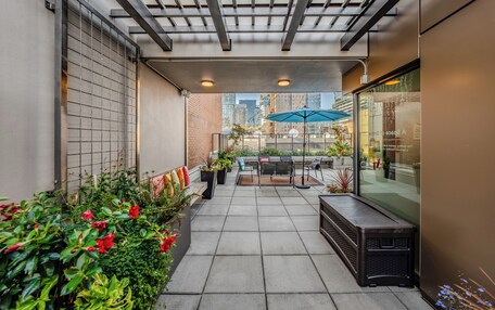 A covered patio with a seating area, potted plants, and a view of the cityscape.