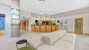 A reception area with a wooden desk, a white sofa, and a pillar with a colorful design. - Hotel Willo (formerly YWCA Hotel Vancouver) (Vancouver)
