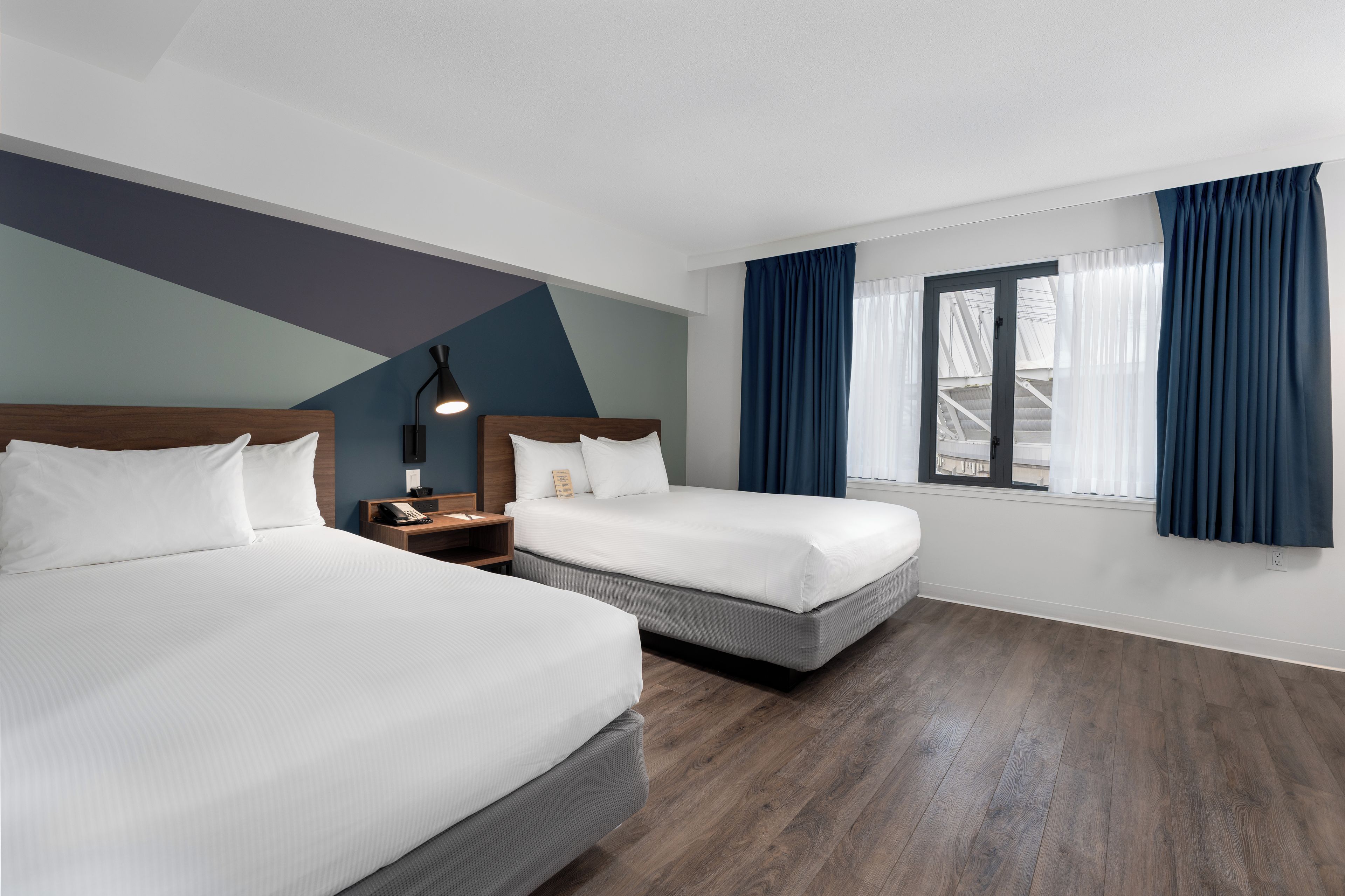 Een hotelkamer met twee bedden, een bureau, een lamp en een raam met gordijnen.