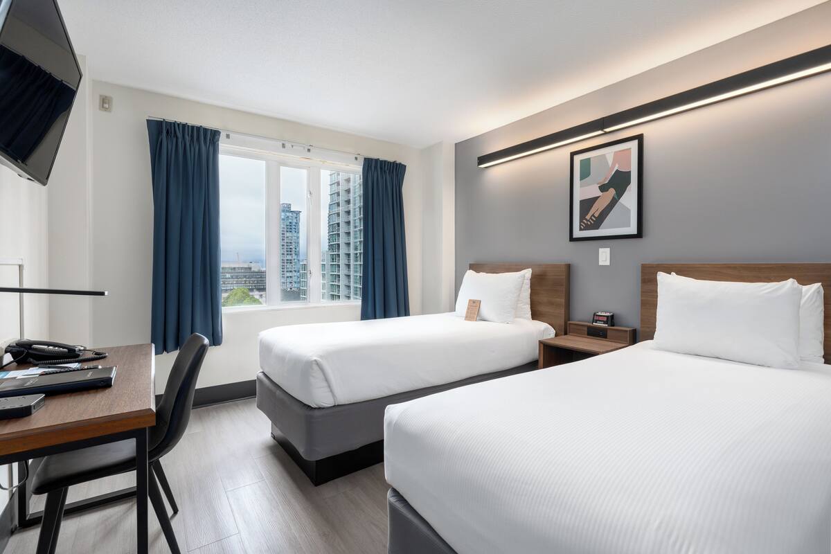 Une chambre d’hôtel avec deux lits, un bureau avec une chaise, une télévision et une fenêtre avec des rideaux.