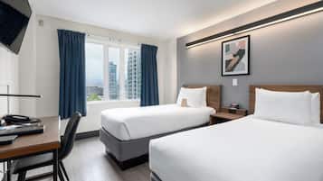 A hotel room with two beds, a desk with a chair, a TV, and a window with curtains.