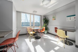 A modern dining area with a glass table, colorful chairs, and a large window with a view of a bridge. - Hotel Willo (formerly YWCA Hotel Vancouver) (Vancouver)