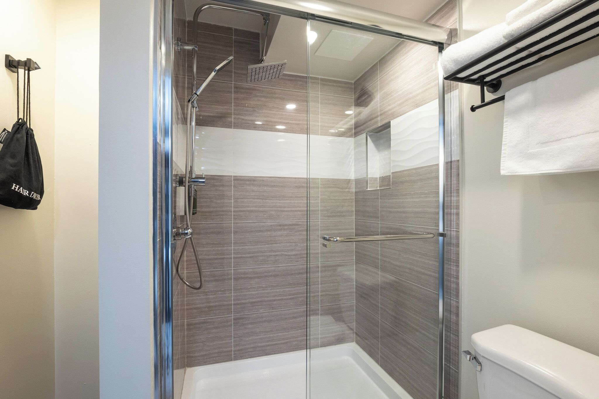 A modern bathroom with a glass-enclosed shower, a white toilet, and a towel rack with a white towel.