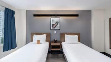 Une chambre d’hôtel avec deux lits simples, une table de chevet, un tableau encadré au mur et une fenêtre avec des rideaux.