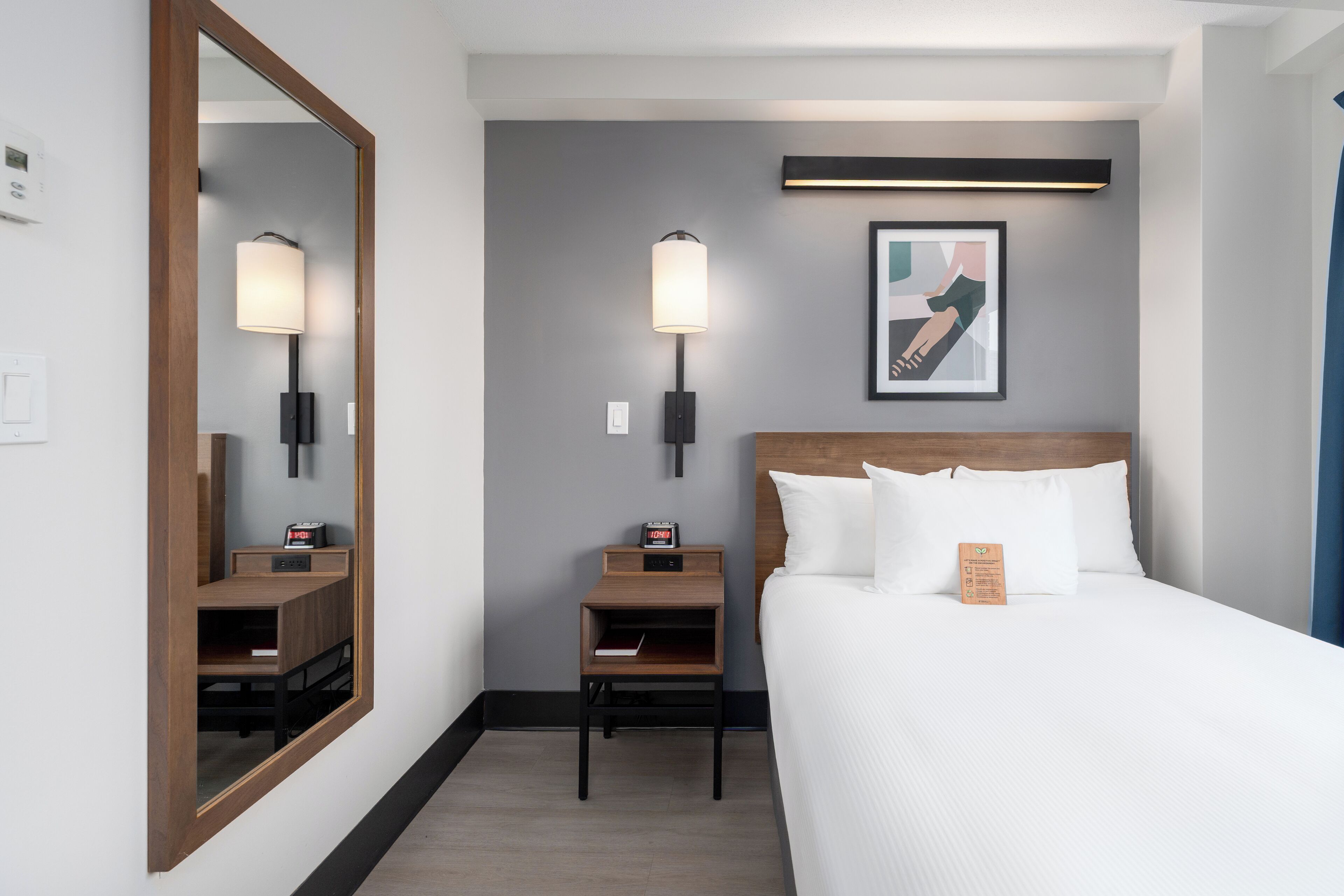 Hotelkamer met een groot bed, nachtkastje, een wandlamp, een ingelijst kunstwerk en een spiegel.