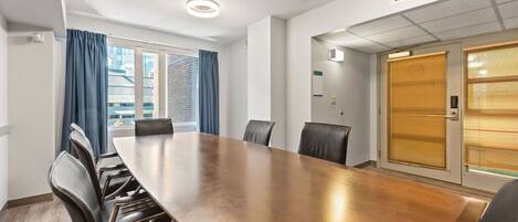A conference room with a long table and chairs, a window with curtains, and a door with blinds.