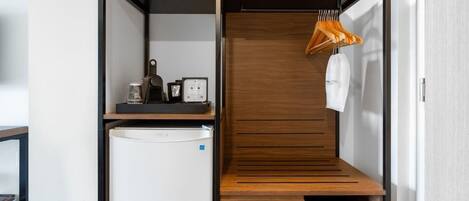 A compact room with a built-in wardrobe, a small kitchenette, and a hanging coat rack.