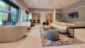 A spacious living area with a large window, a sofa set, a coffee table, and a TV mounted on the wall. - Hotel Willo (formerly YWCA Hotel Vancouver) (Vancouver)