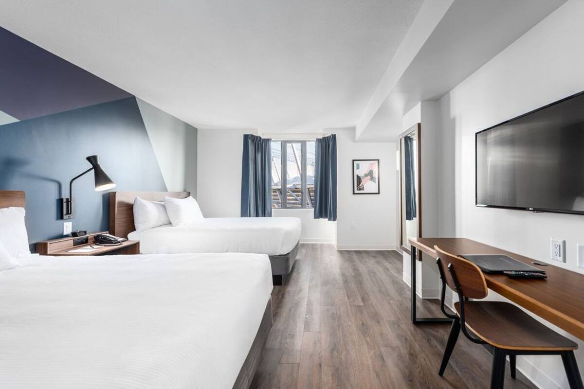Une chambre d’hôtel avec deux lits, un bureau, une chaise, une télévision et une fenêtre avec des rideaux.
