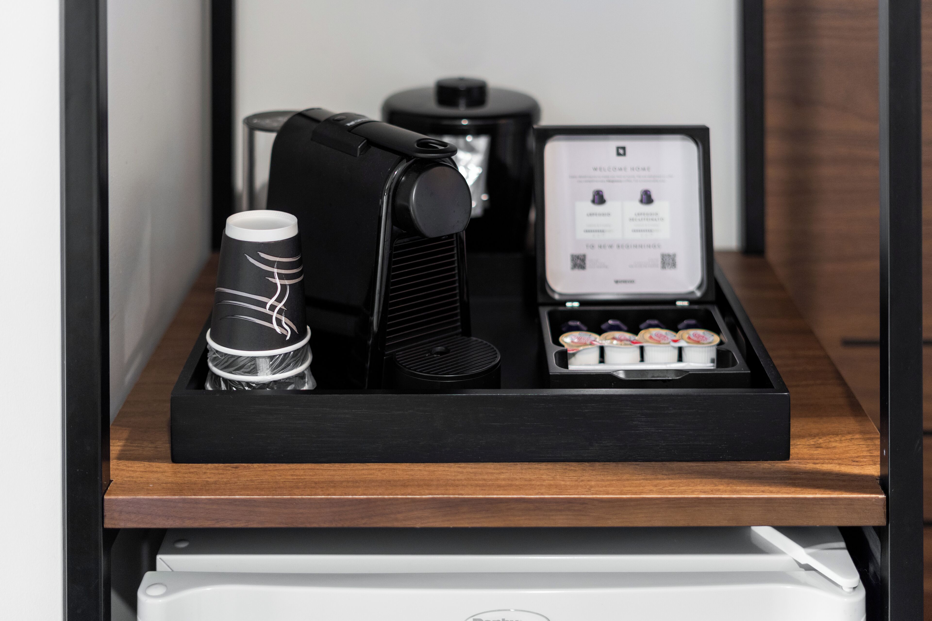 A black coffee machine and a coffee pod holder on a wooden shelf.