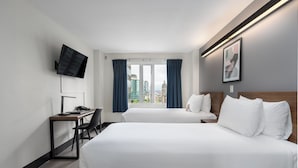 A hotel room with two beds, a desk with a chair, a flat-screen TV mounted on the wall, and a large window with curtains. - Hotel Willo (formerly YWCA Hotel Vancouver) (Vancouver)