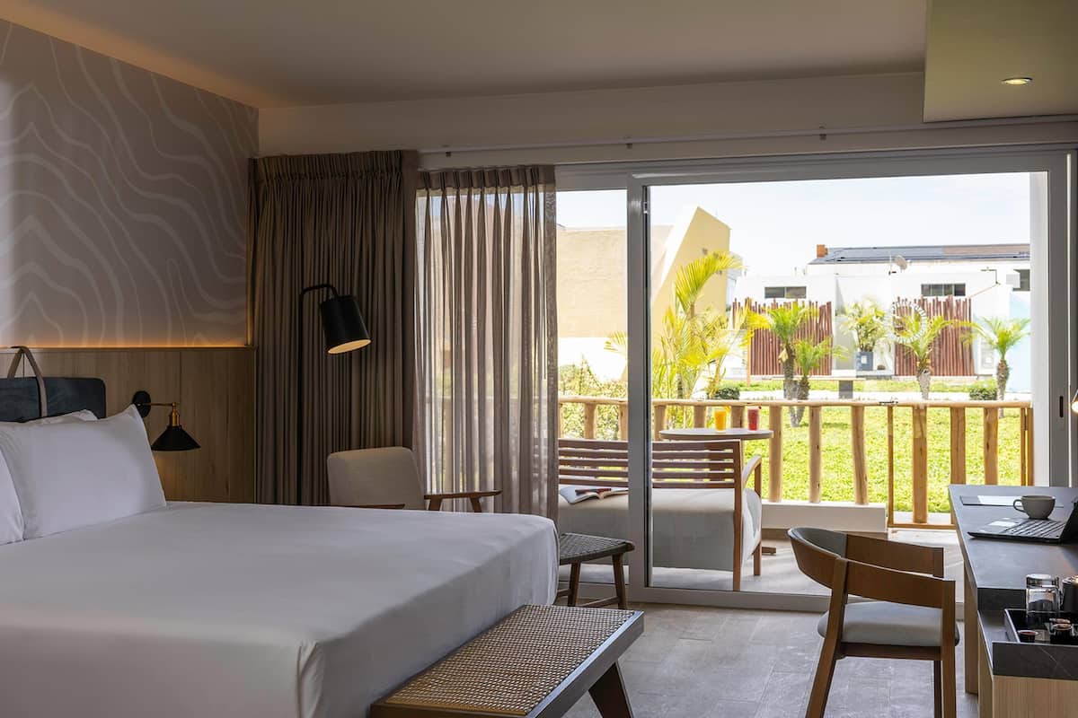 A hotel room with a bed, a desk, a chair, a laptop, and a view of the outdoor area.