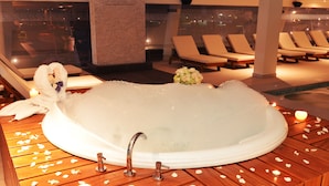 A spa area with a hot tub surrounded by wooden flooring, lounge chairs, and candles. - Aranwa Paracas Resort & Spa (Paracas)