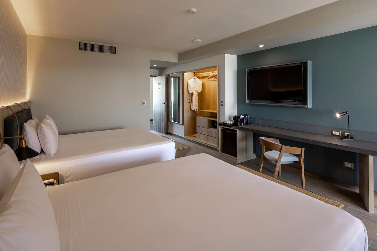 A hotel room with two beds, a TV, a desk with a chair, and a walk-in closet.
