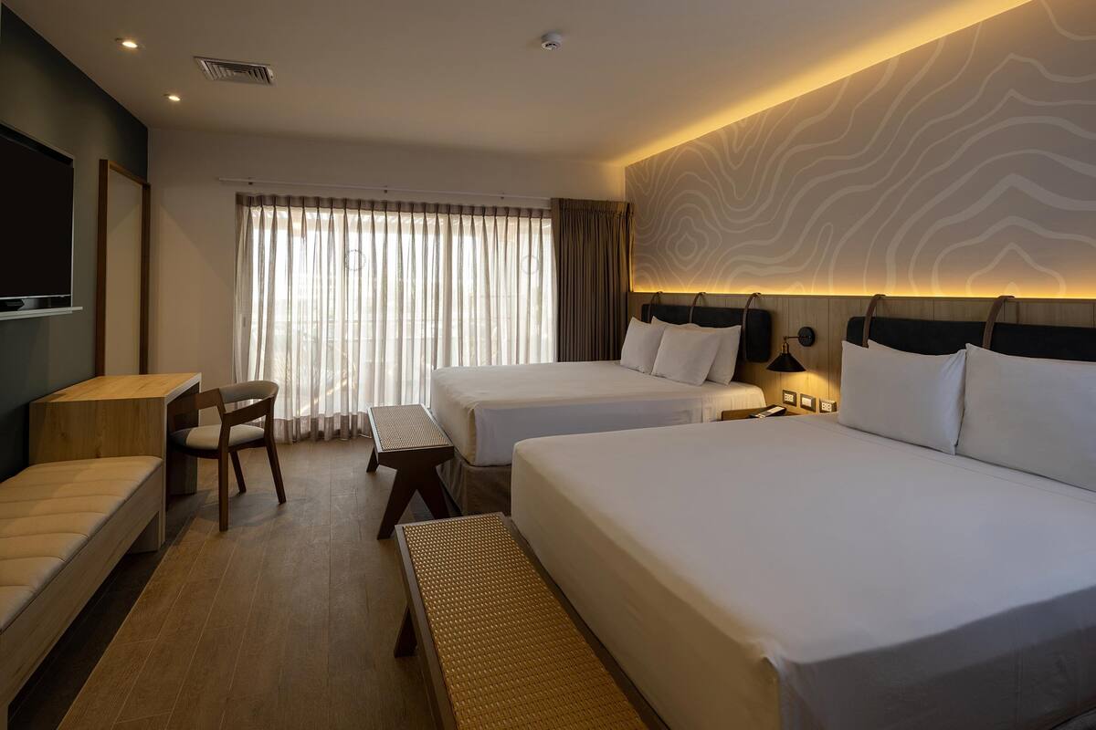 A hotel room with two beds, a desk, a chair, and a large window with curtains.
