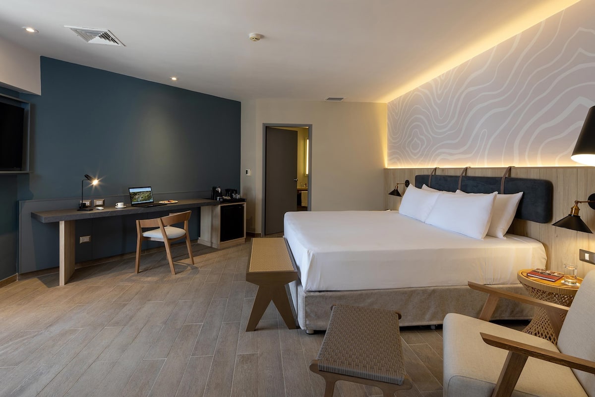A modern hotel room with a bed, desk, and seating area.