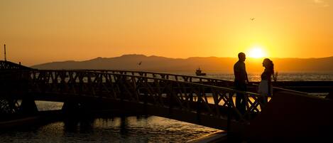 A sunset over a bridge with two people standing on it.