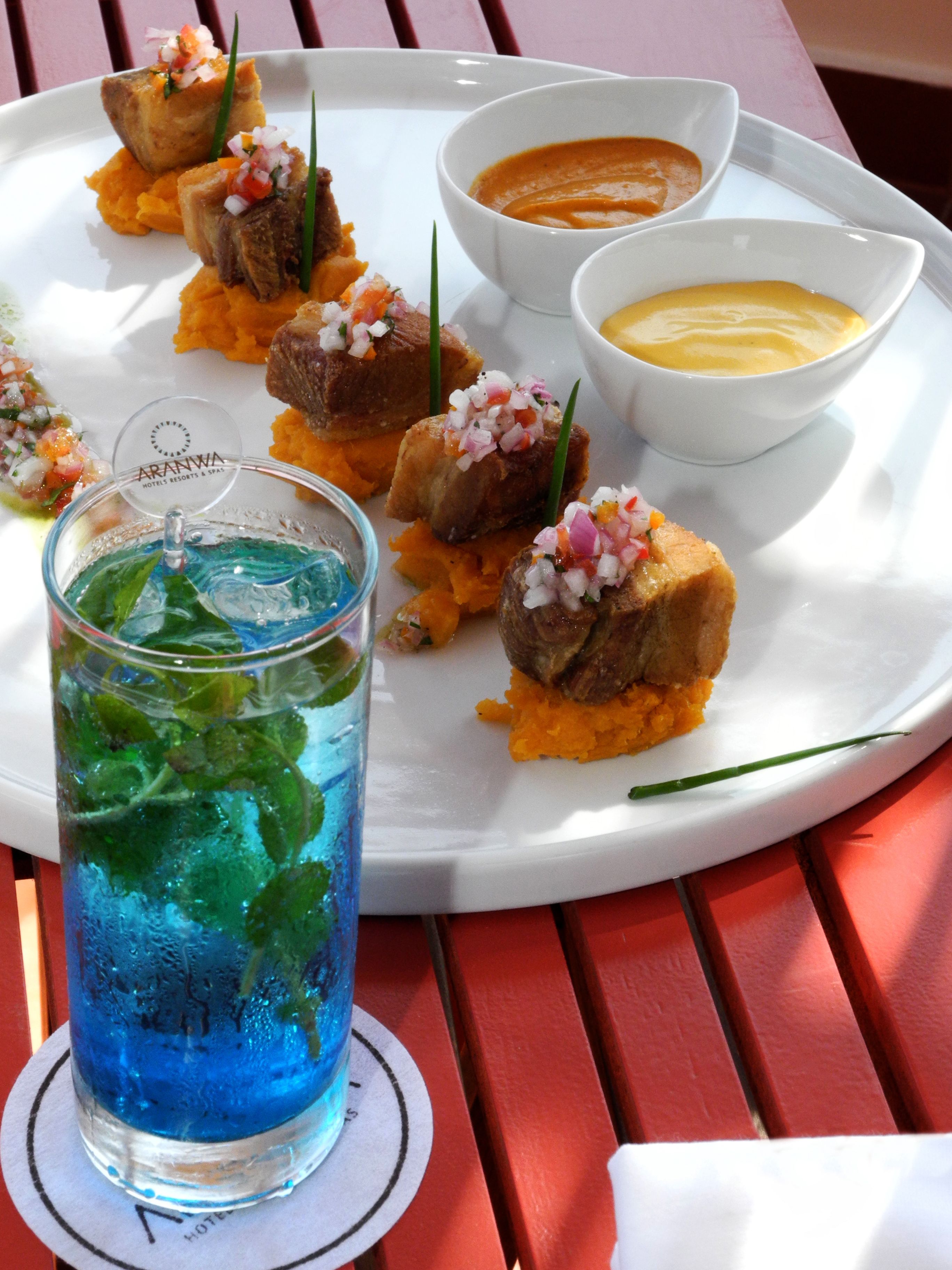 Un plato blanco con alimentos y dos recipientes pequeños de salsa, un vaso de bebida azul y un posavasos con la marca del hotel.