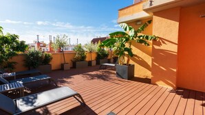 Een terras op het dak met houten vloer, lounge stoelen en plantenbakken.