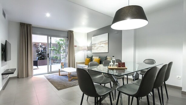 Een moderne eetruimte met een glazen tafel en zwarte stoelen, een hanglamp en een schuifdeur van glas die uitkomt op een balkon.