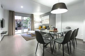 Un comedor moderno con una mesa de vidrio y sillas negras, una lámpara colgante y un amplio ventanal corredizo que da a un balcón.