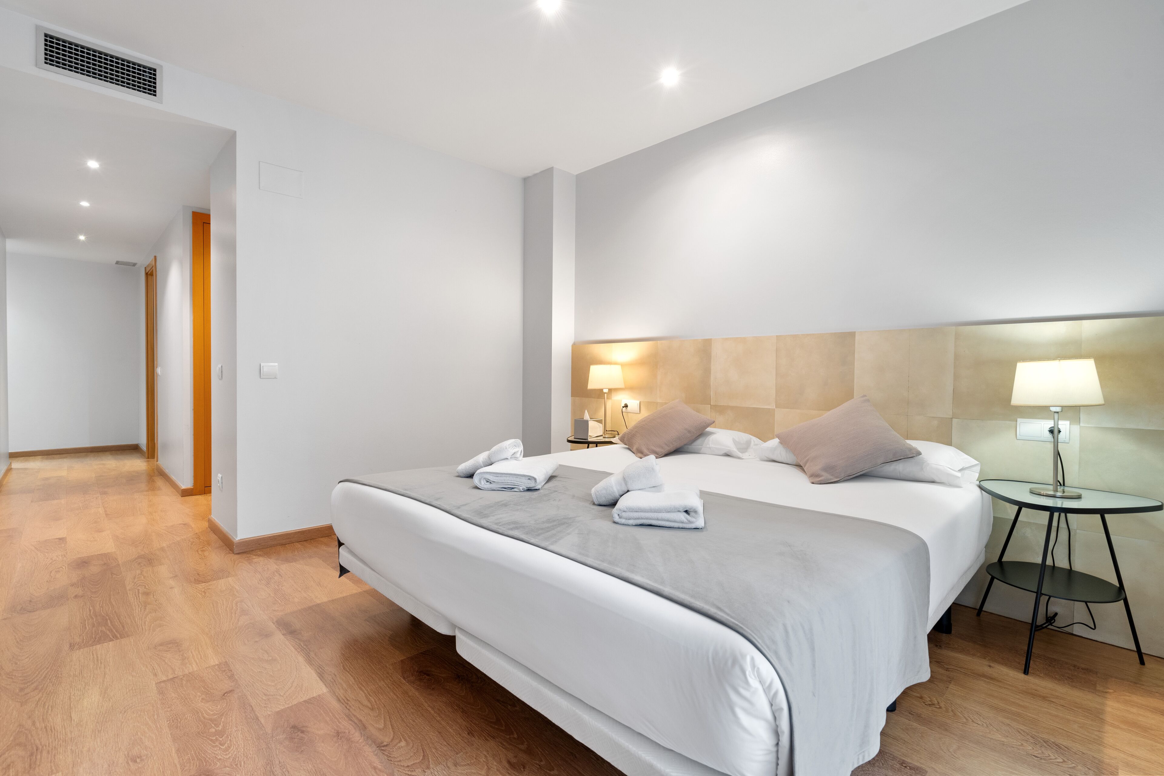 A modern hotel room with a large bed, a bedside table with a lamp, and a small round table.