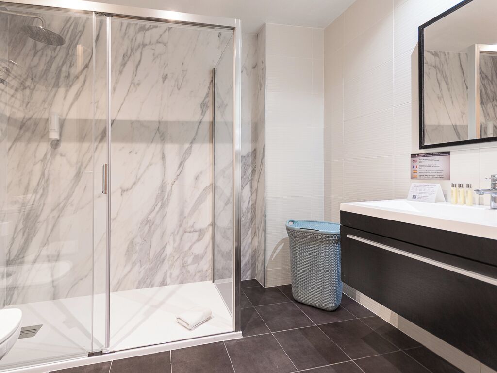 A modern bathroom with a glass-enclosed shower, a white sink, and a large mirror.