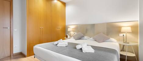 Una habitación de hotel moderna con una cama grande, dos mesitas de noche con lámparas, un armario de madera y una decoración en tonos neutros.