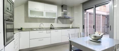 A modern kitchen with white cabinets, a stainless steel range hood, and a dining area with a table and chairs.