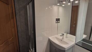 Un baño moderno con cabina de ducha de vidrio, un lavabo blanco y un espejo.