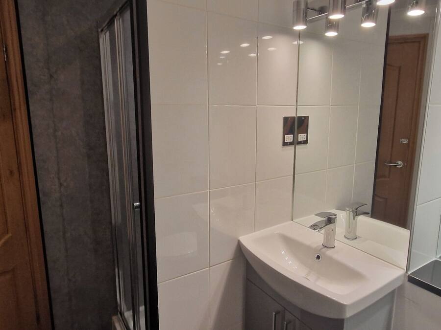 Une salle de bain moderne avec une douche à parois de verre, un lavabo blanc et un miroir.