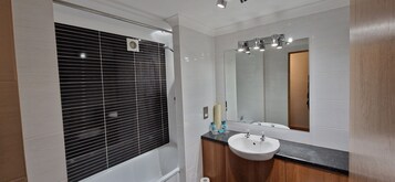 A modern bathroom with a black-tiled shower enclosure, a white sink with a wooden vanity, and a large mirror above the sink.