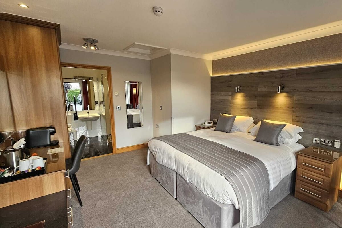 A modern hotel room with a large bed, bedside tables, a desk with a chair, and a mirror.