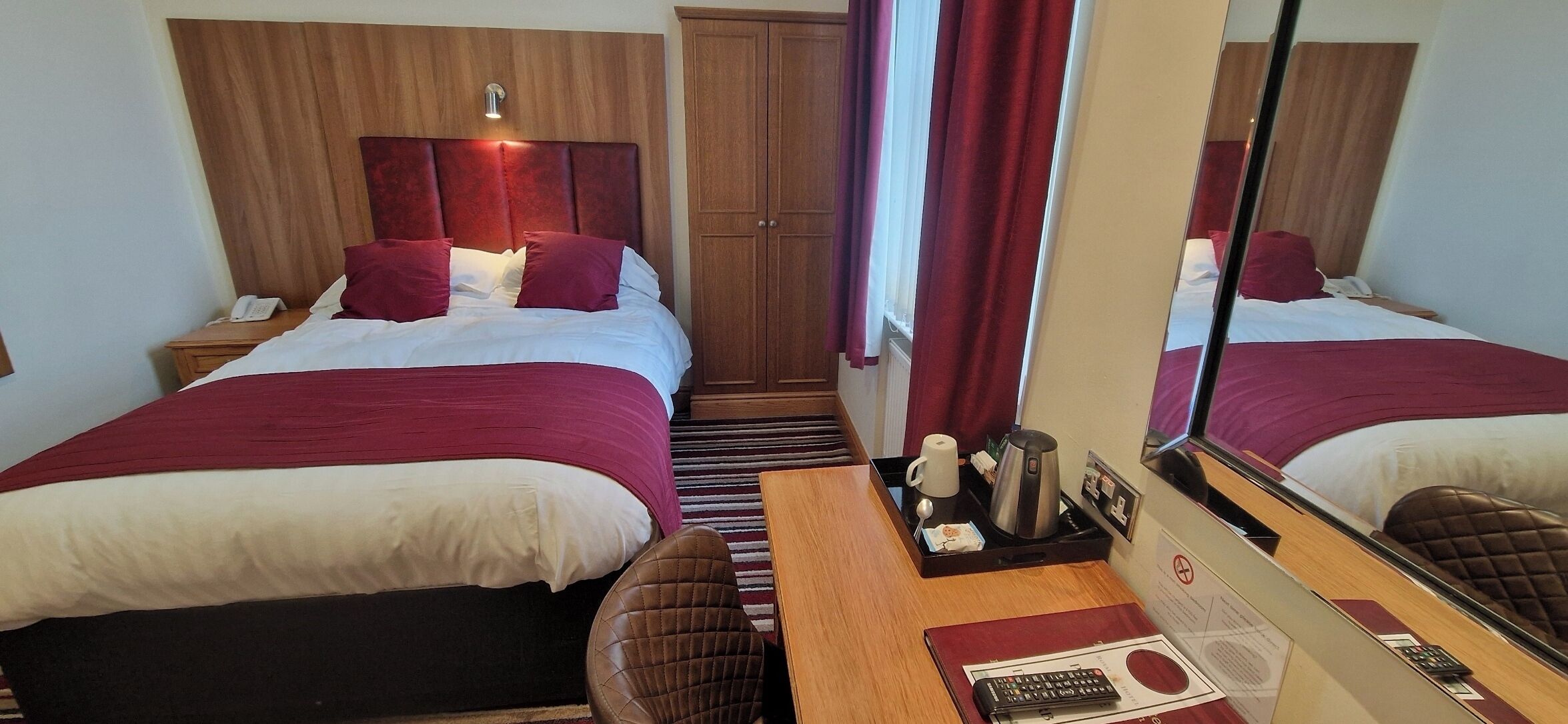 A hotel room with two beds, a wooden headboard, a nightstand, a mirror, and a tray with a coffee pot and other items.