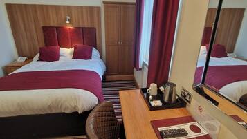 A hotel room with two beds, a wooden headboard, a nightstand, a mirror, and a tray with a coffee pot and other items.