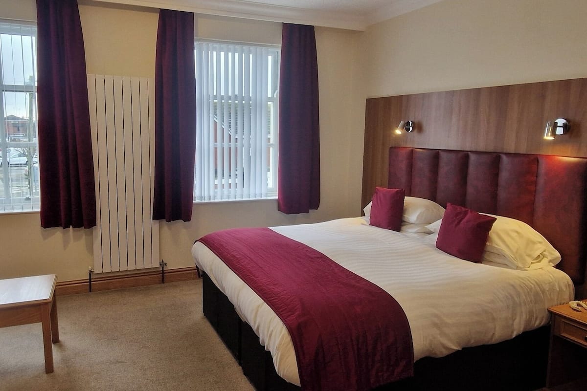 A hotel room with a large bed, a bedside table, a chair, a window with curtains, and a view of a parking lot.