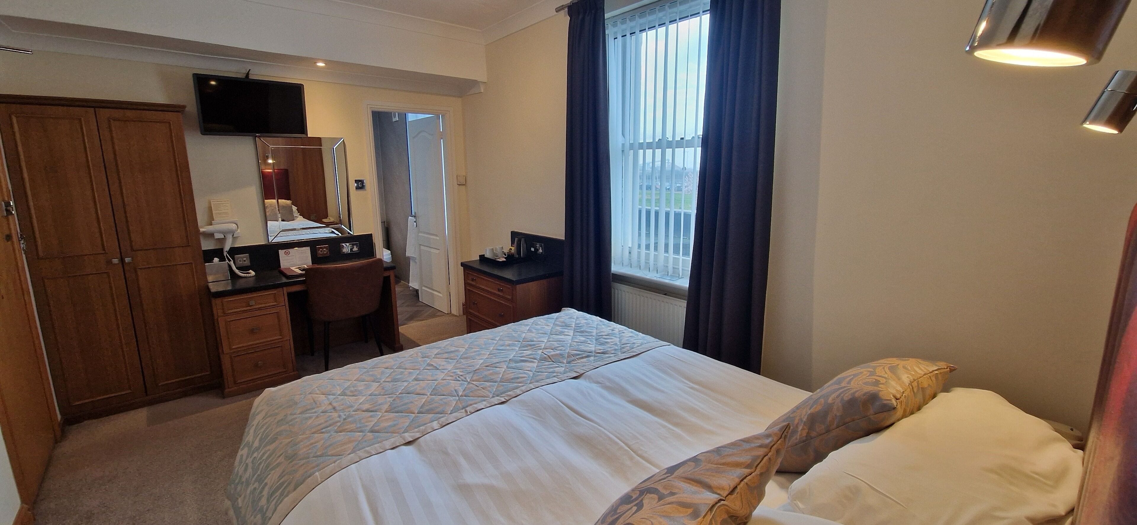 A hotel room with a bed, a desk, a chair, a wardrobe, a television, and a window with curtains.