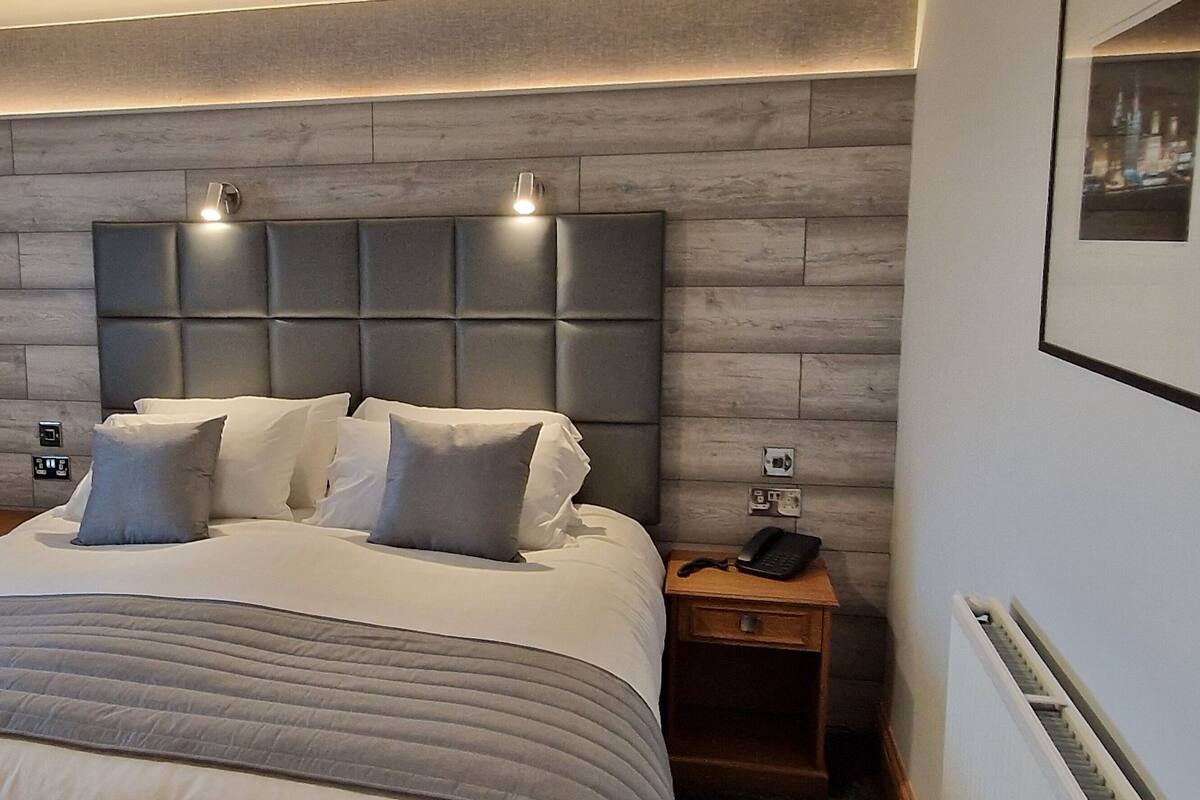 A modern bedroom with a large bed, a wooden wardrobe, a bedside table with a lamp, and a framed picture on the wall.
