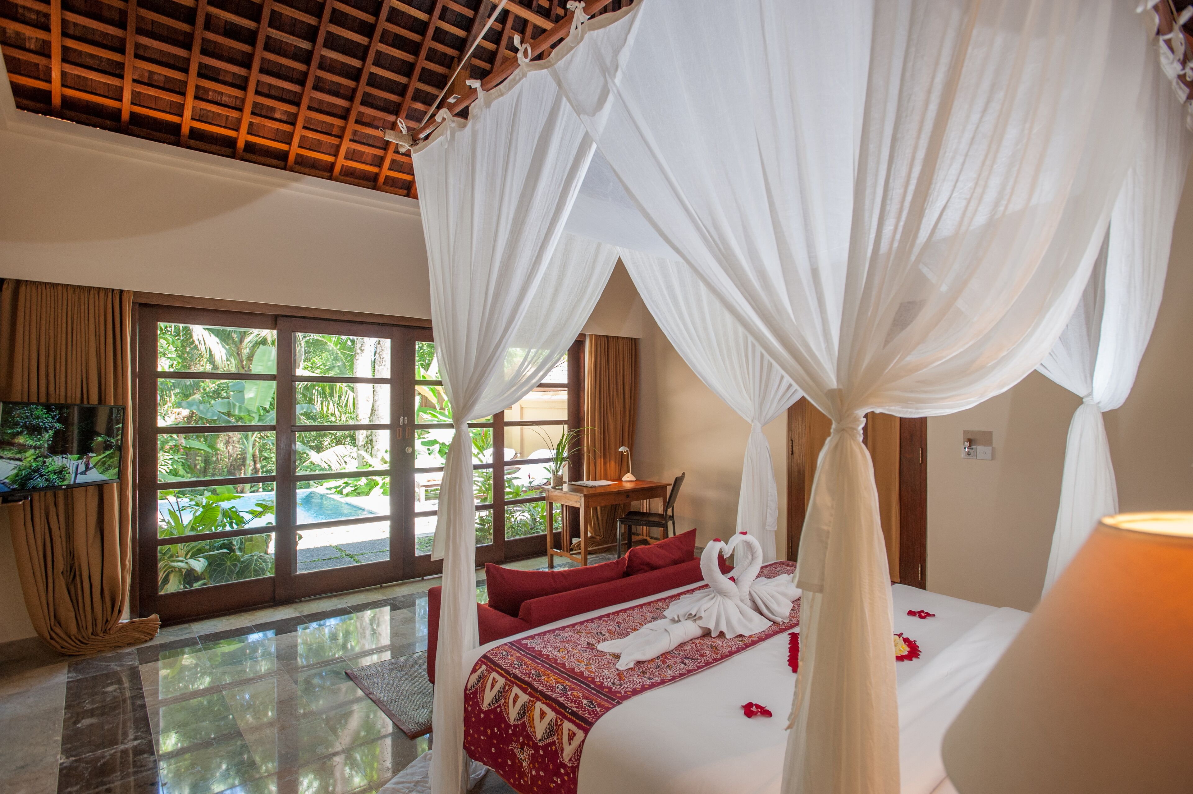Una habitación con cama, televisión, escritorio y vista a zonas verdes.