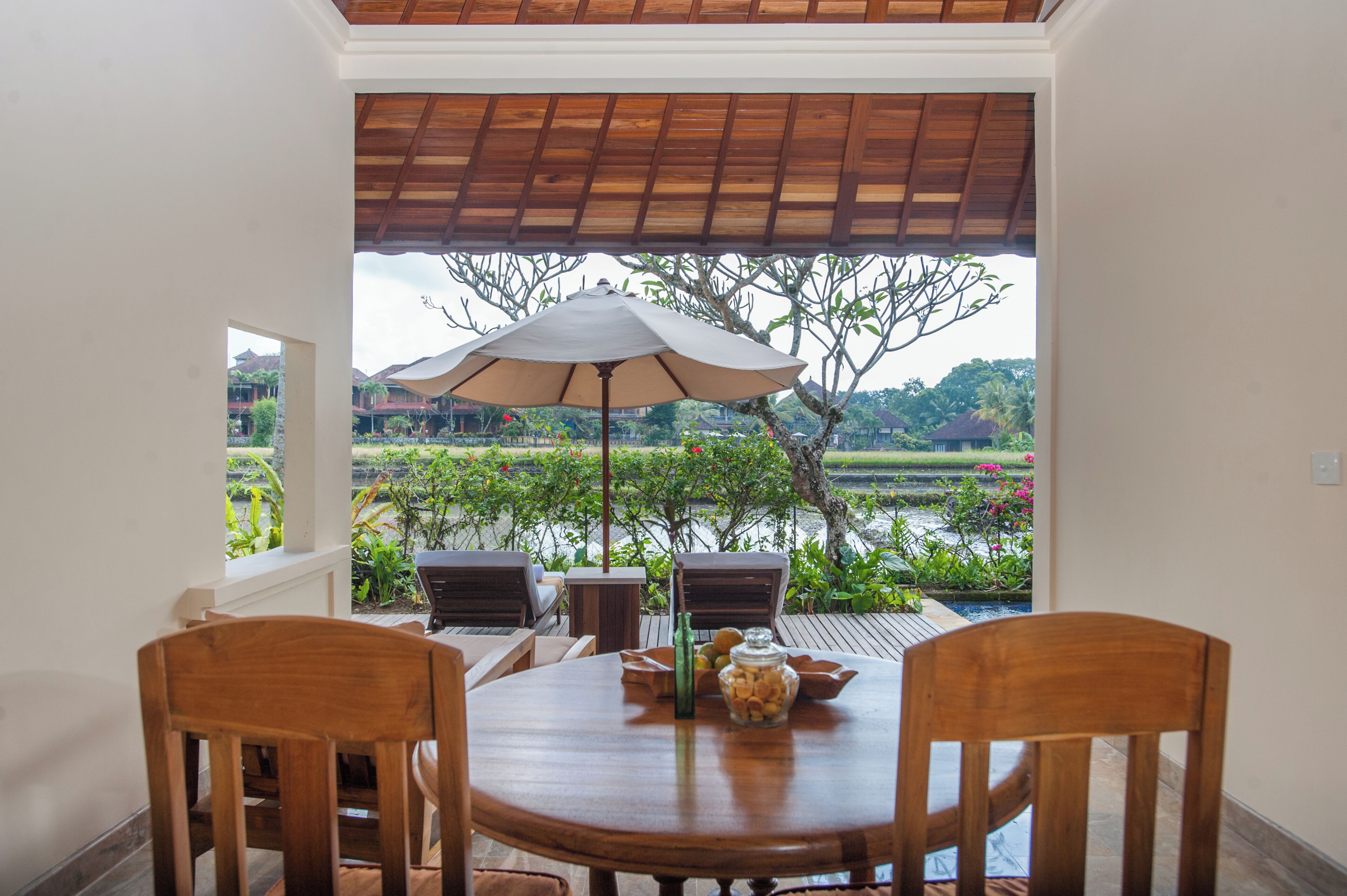 Un comedor con una mesa y sillas, un paraguas y vistas a un jardín y edificios.