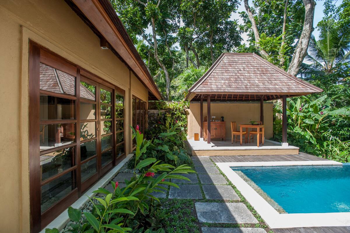 A house with a swimming pool, a covered patio, and a garden with tropical plants.