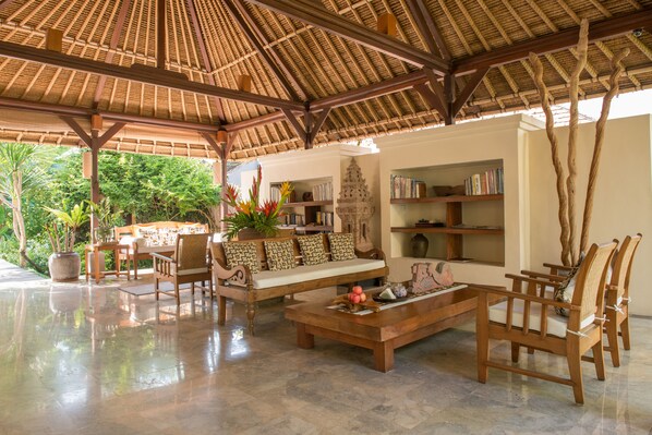 A spacious indoor area with a thatched roof, wooden furniture, and a bookshelf.