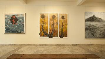 A gallery with three paintings on the wall and a wooden bench in the foreground.