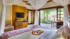 Un dormitorio con cama, televisor, escritorio y vista a zonas verdes.